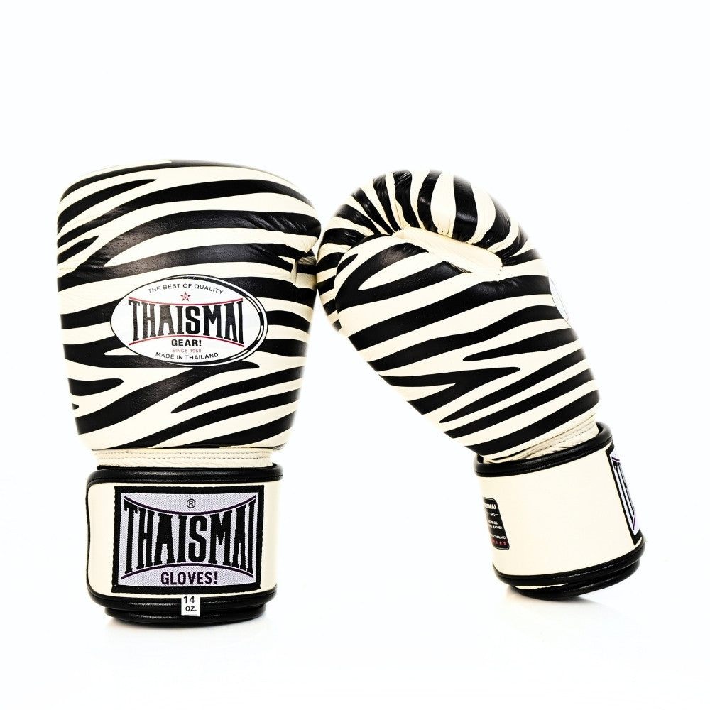 Angled view of white and black ThaiSmai FBG124-Zebra Muay Thai boxing gloves showing the zebra-striped padded knuckles, ergonomic glove shape and hook-and-loop wrist closures on a white background