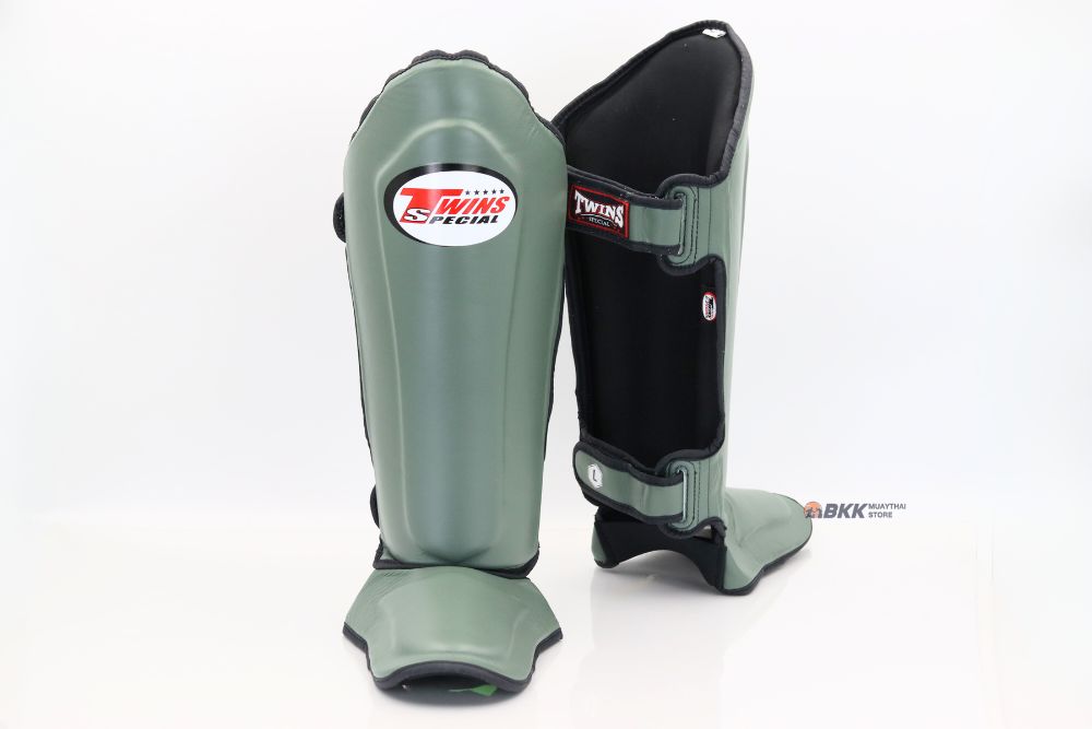 Angled view of gray-green and black Twins Special SGL-10 shin guards showing full-length shin and instep padding, contoured protection, and secure hook-and-loop straps for Muay Thai and kickboxing on a white background