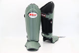 Angled view of gray-green and black Twins Special SGL-10 shin guards showing full-length shin and instep padding, contoured protection, and secure hook-and-loop straps for Muay Thai and kickboxing on a white background
