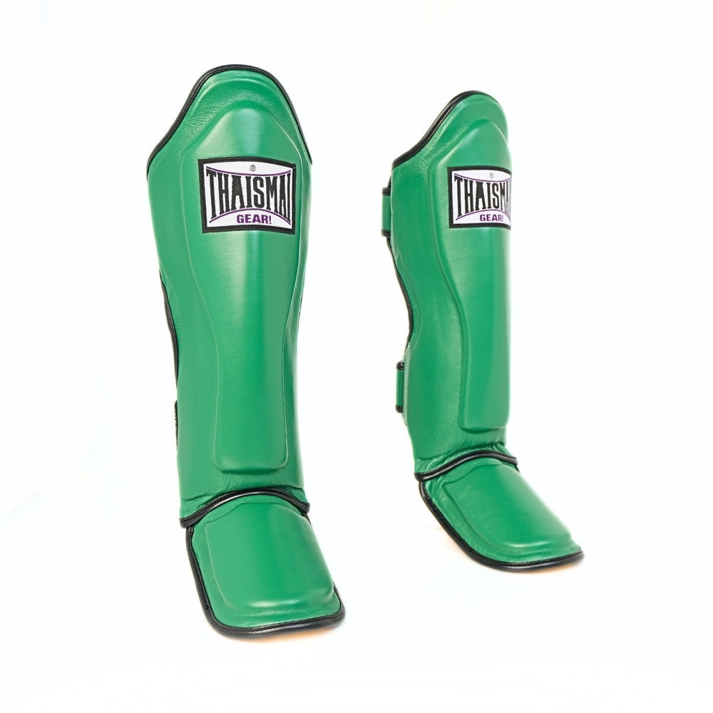 Three-quarter view of the green THAISMAI LP184 Muay Thai shin guards, showing the padded shin fronts, foot guards, curved profile and black trim against white.