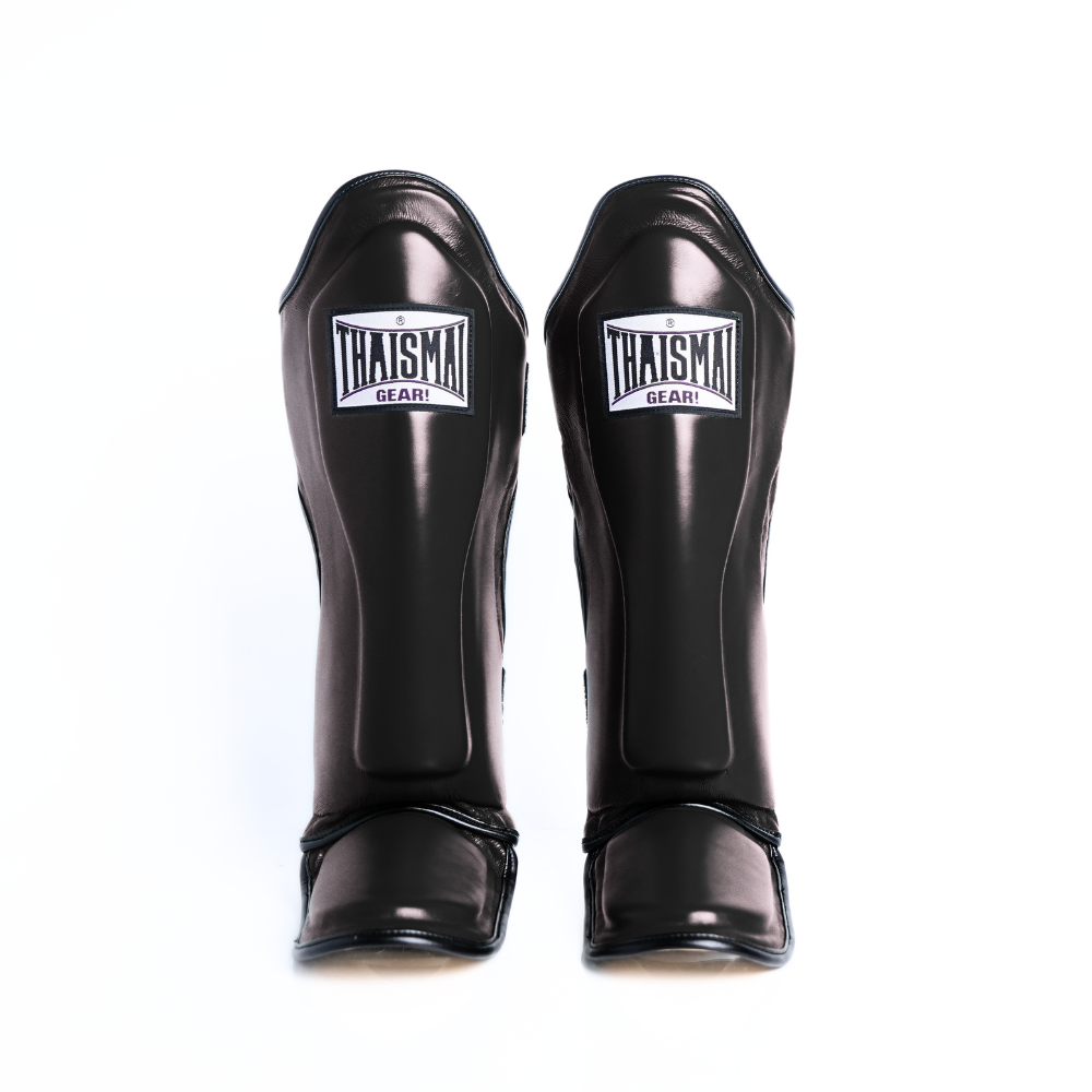 Front view of the black THAISMAI LP184 Muay Thai shin guards, showing the pair’s padded shin panels, THAISMAI Gear logos and protective foot sections on white.