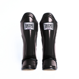 Front view of the black THAISMAI LP184 Muay Thai shin guards, showing the pair’s padded shin panels, THAISMAI Gear logos and protective foot sections on white.