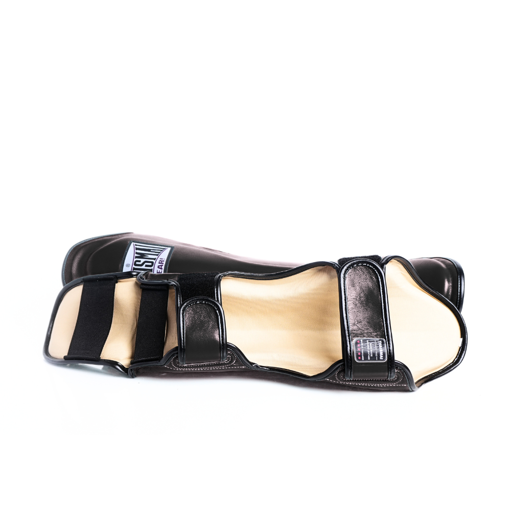 Side view of the black THAISMAI LP184 shin guard laid flat, showing the padded shell, light-colored inner lining and adjustable hook-and-loop fastening straps.