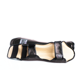 Side view of the black THAISMAI LP184 shin guard laid flat, showing the padded shell, light-colored inner lining and adjustable hook-and-loop fastening straps.