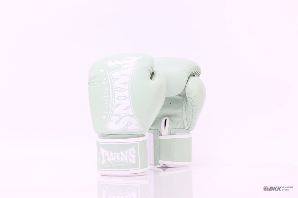 Pair of mint green Twins Special boxing gloves with white branding and hook-and-loop wrist straps displayed on a reflective white surface