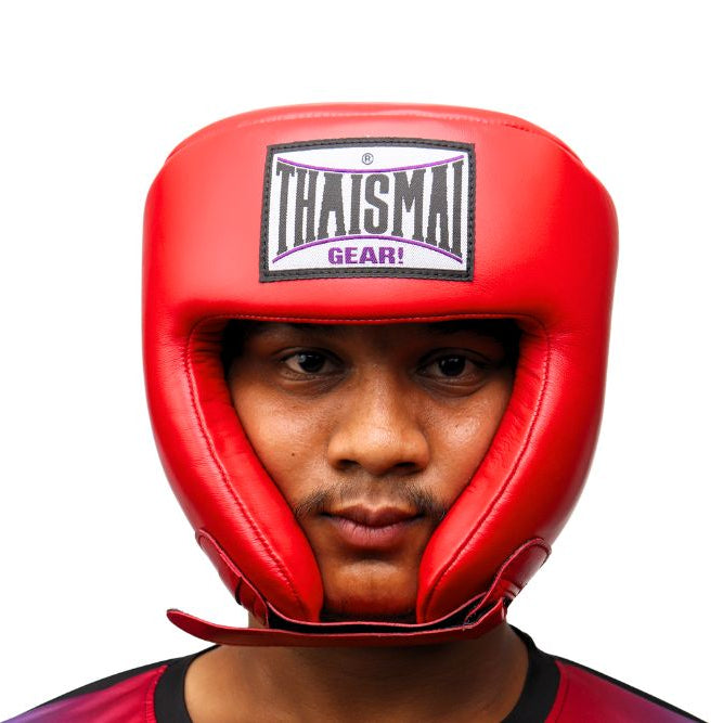 Front view of a person wearing the red THAISMAI HG-152 head guard, showing the brow logo, face opening and padded chin strap against a white background.