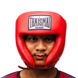Front view of a person wearing the red THAISMAI HG-152 head guard, showing the brow logo, face opening and padded chin strap against a white background.