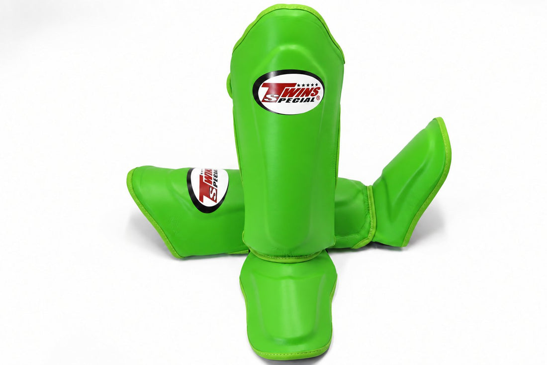 Front view of green Twins Special SGL-10 shin guards arranged to show full-length shin and instep padding, secure hook-and-loop straps, and padded foot support for Muay Thai and kickboxing on a white background