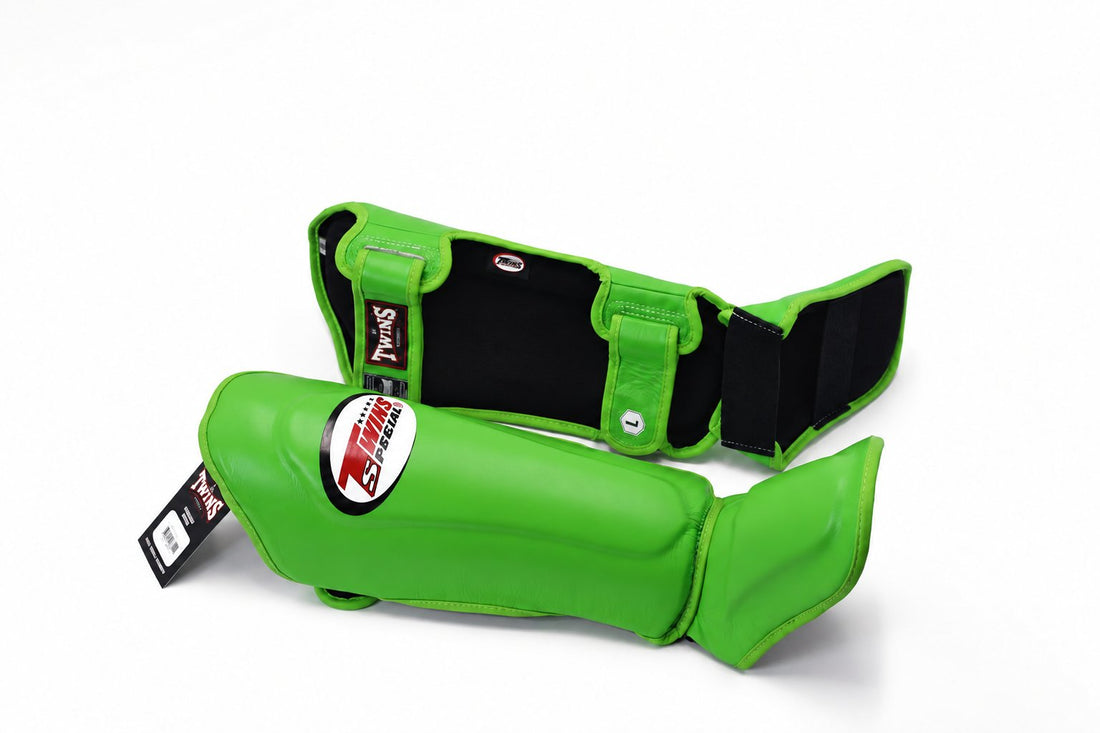 Angled view of green Twins Special SGL-10 shin guards showing contoured shin and instep padding, wide hook-and-loop closures, and padded foot support for Muay Thai and kickboxing on a white background