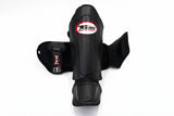 Front view of black Twins Special SGL-10 shin guards showing full-length shin and instep padding, secure hook-and-loop straps, and padded foot support for Muay Thai and kickboxing on a white background