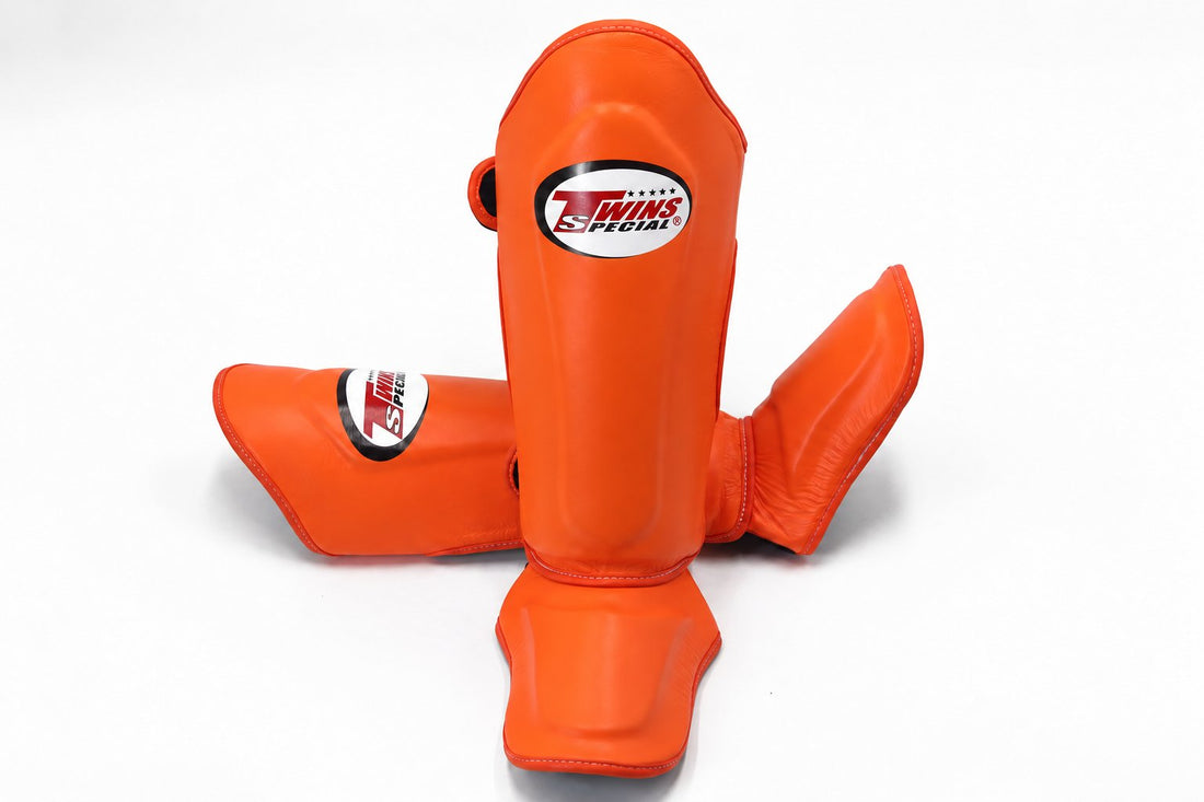 Twins Special SGL-10 shin guards in black synthetic leather with full-length shin and instep protection, secure hook-and-loop straps and padded support for Muay Thai and kickboxing training on a white background