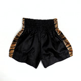 Angled view of black and yellow ThaiSmai TIGER Muay Thai shorts showing the tiger artwork, satin fabric, side slits and drawstring waistband on a white background