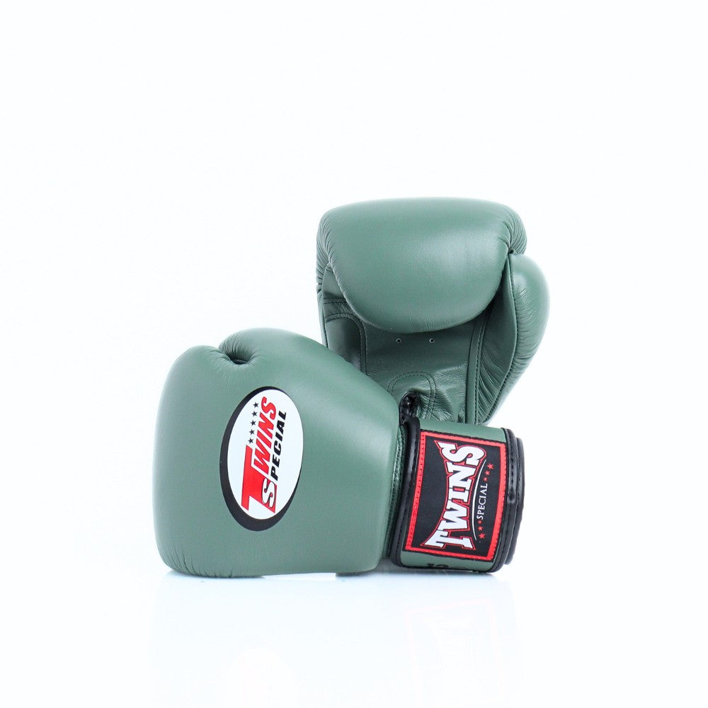 Pair of olive green Twins Special boxing gloves arranged at an angle, with the front glove showing the Twins logo and branded wrist patch on a white background