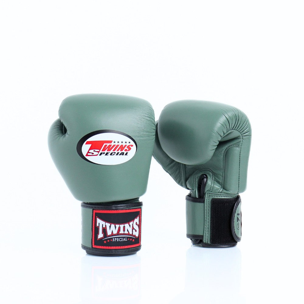 Pair of olive green Twins Special boxing gloves showing the front logo and rear glove with black hook-and-loop wrist strap and branded wrist patch on a white background