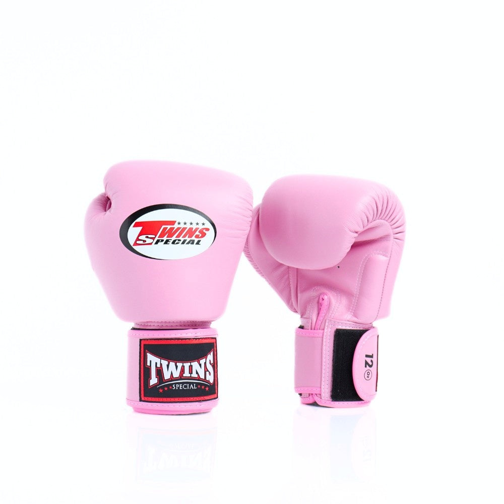 Pair of pink Twins Special boxing gloves showing the front logo and rear glove with black hook-and-loop strap and 12 oz marking on a white background