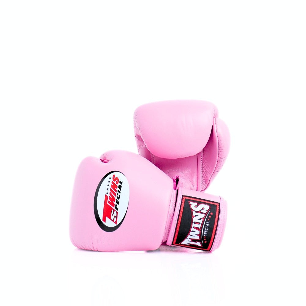 Pair of pink Twins Special boxing gloves arranged at an angle, with the front glove showing the Twins logo and pink wrist patch on a white background