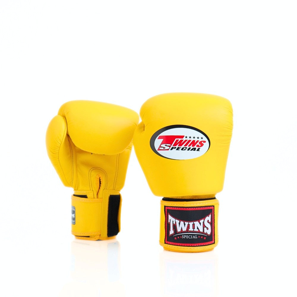 Pair of bright yellow Twins Special boxing gloves showing front and rear views with the Twins logo, wrist patch and hook-and-loop strap on a white background