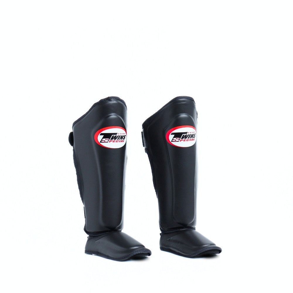 Twins Special SGL-10 shin guards in black synthetic leather with full-length shin and instep protection, secure hook-and-loop straps and padded support for Muay Thai and kickboxing training on a white background