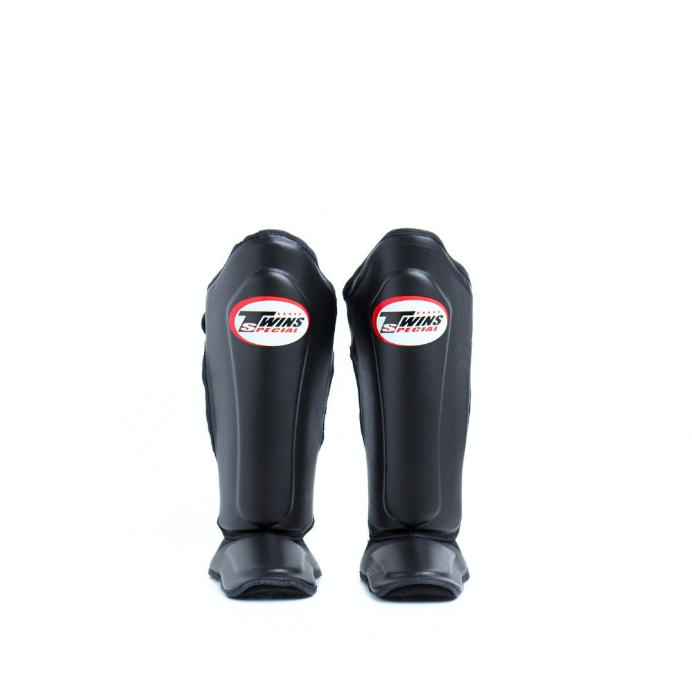 Twins Special SGL-10 shin guards in black synthetic leather with full-length shin and instep protection, secure hook-and-loop straps and padded support for Muay Thai and kickboxing training on a white background