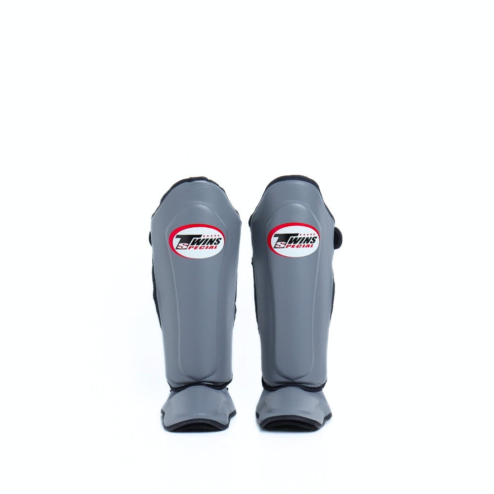 Twins Special SGL-10 shin guards in black synthetic leather with full-length shin and instep protection, secure hook-and-loop straps and padded support for Muay Thai and kickboxing training on a white background