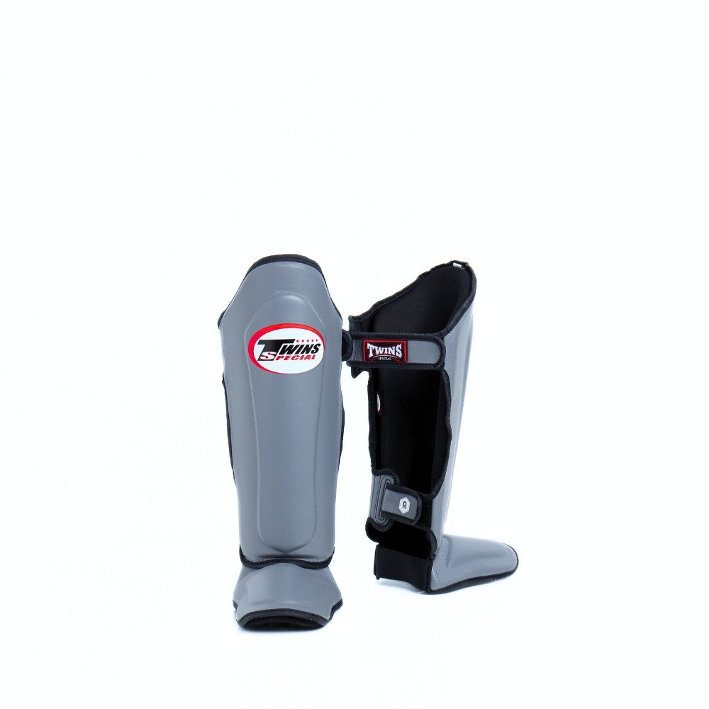 Twins Special SGL-10 shin guards in black synthetic leather with full-length shin and instep protection, secure hook-and-loop straps and padded support for Muay Thai and kickboxing training on a white background