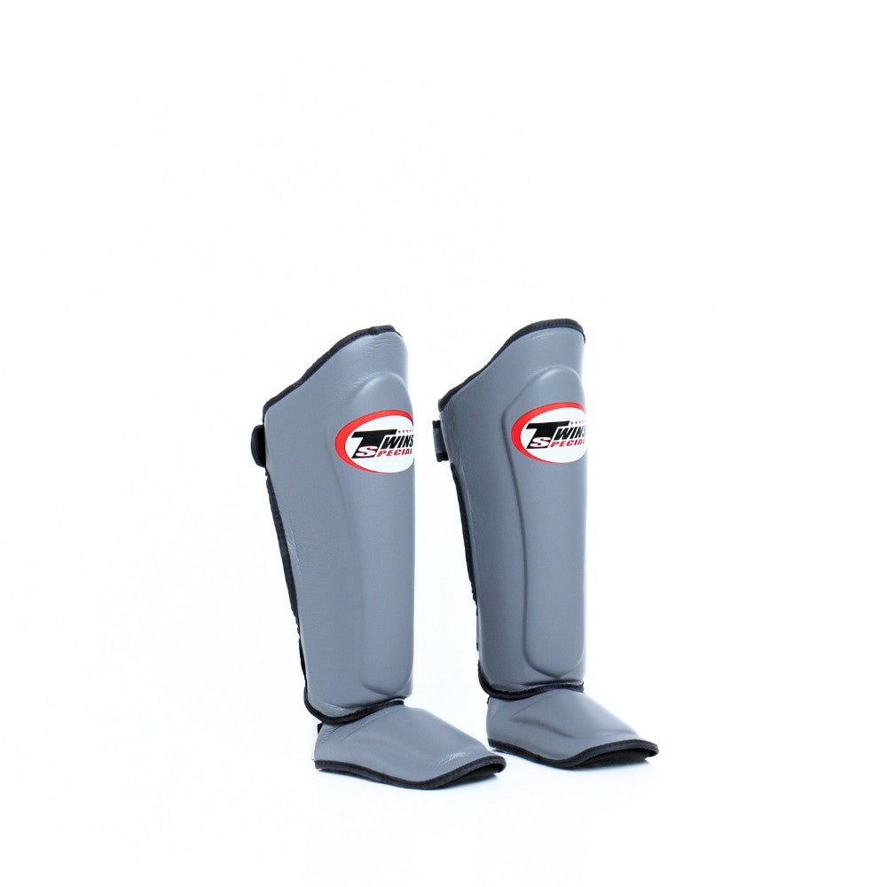 Twins Special SGL-10 shin guards in black synthetic leather with full-length shin and instep protection, secure hook-and-loop straps and padded support for Muay Thai and kickboxing training on a white background