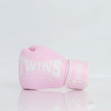 Single light pink Twins Special boxing glove with white branding and hook-and-loop wrist closure resting on a reflective white surface