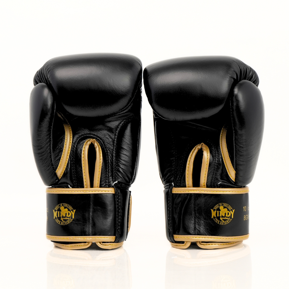 Angled view of Windy BGVH black and gold Muay Thai boxing gloves showing padded knuckles, thumb guard, leather construction and secure wrist closure on a white background