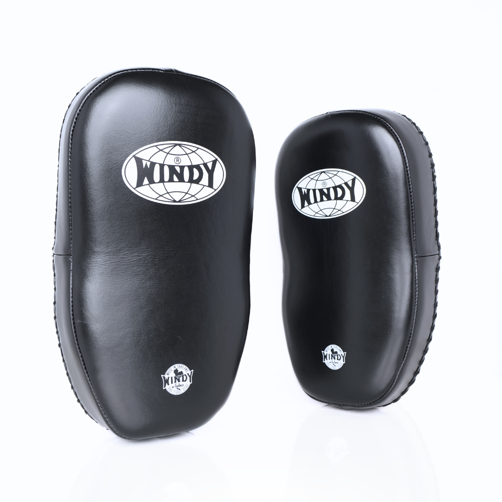 Angled view of black Windy KP-8 leather kick pads showing double straps, curved padding and stitched leather edges on a white background