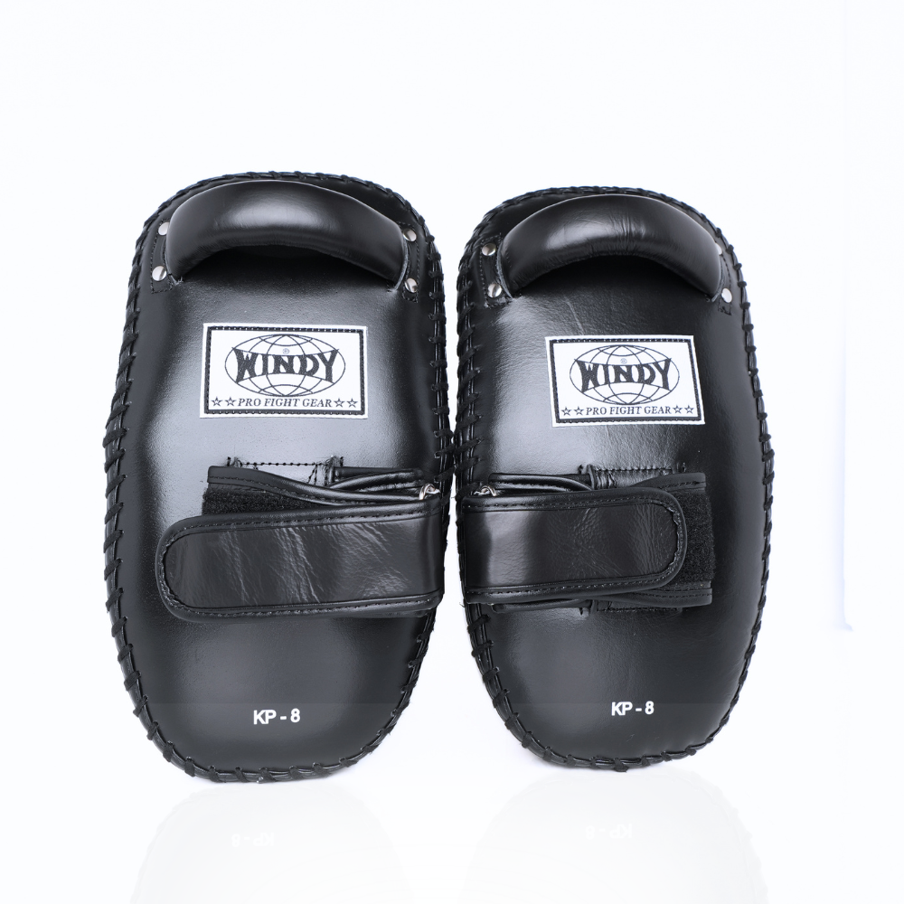 Front view of a pair of black Windy KP-8 leather kick pads with padded striking surfaces, single fastening straps, Windy logos and reinforced stitching for Muay Thai and kickboxing training on a white background