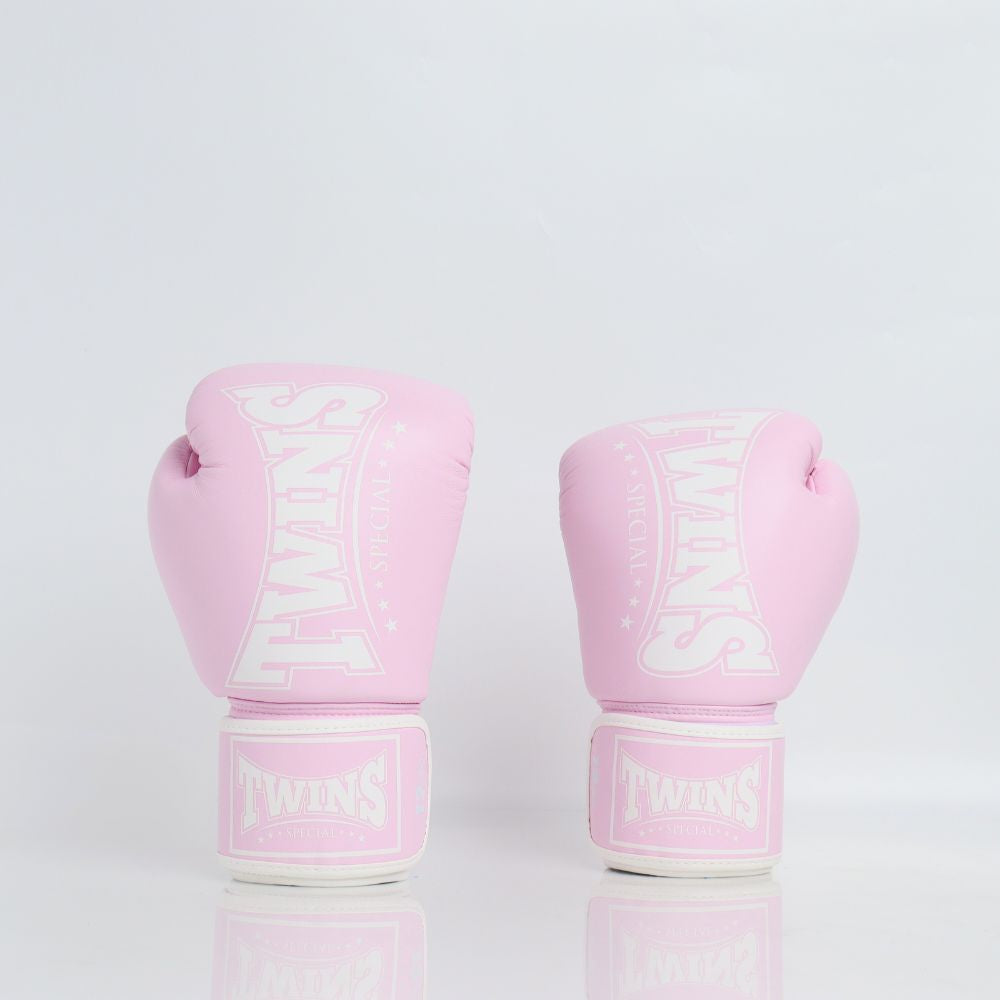 Front view of a pair of light pink Twins Special boxing gloves with white branding and hook-and-loop wrist straps displayed on a reflective white surface