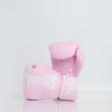 Pair of light pink Twins Special boxing gloves with white branding, open palms and hook-and-loop wrist closures displayed on a reflective white surface
