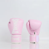 Pair of light pink Twins Special boxing gloves showing front branding and rear hook-and-loop wrist closures on a reflective white surface