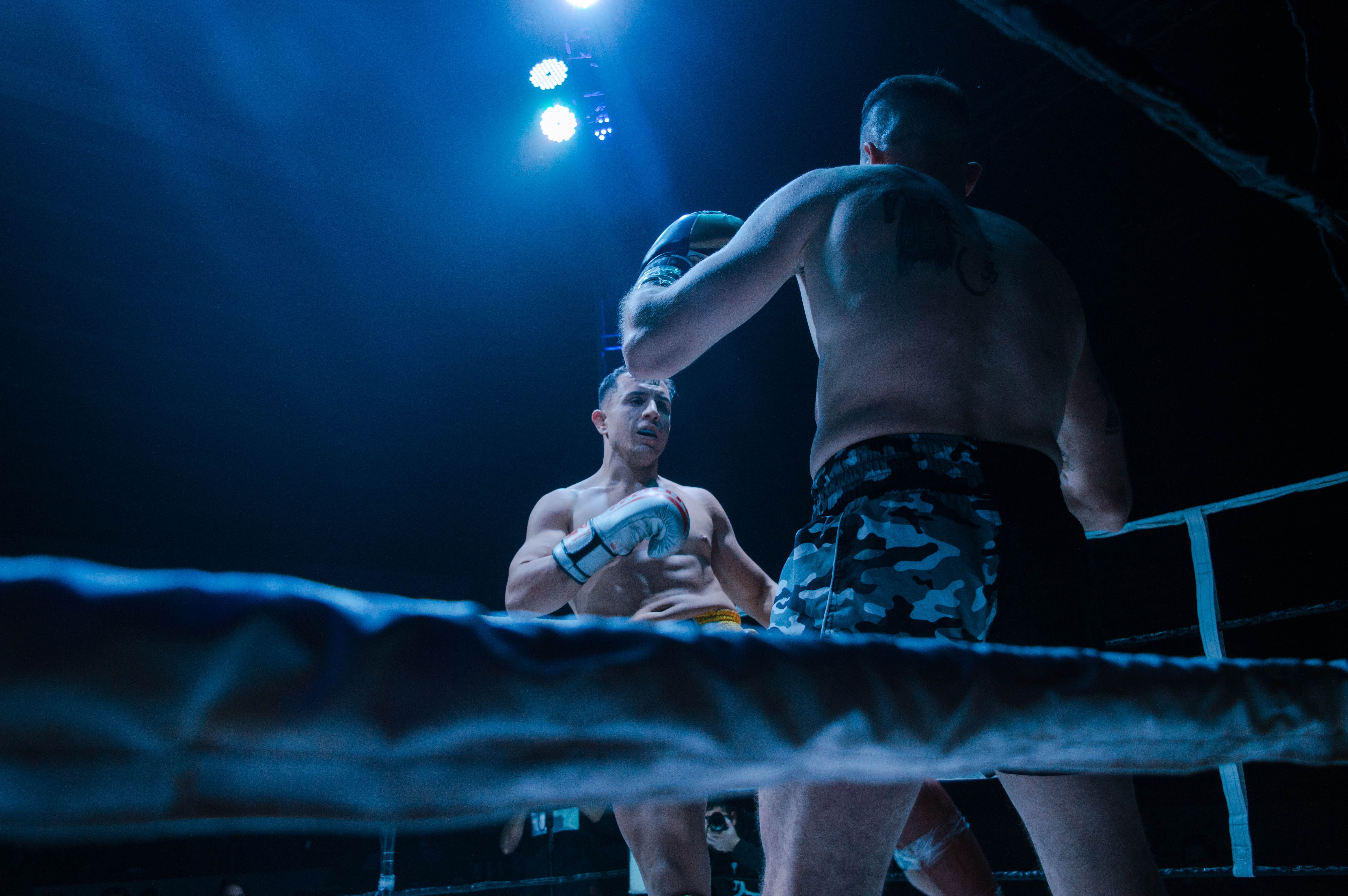 Two Muay Thai fighters facing each other in a boxing ring under blue lights.
